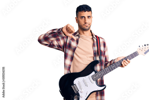Young hispanic man playing electric guitar with angry face, negative sign showing dislike with thumbs down, rejection concept © Krakenimages.com