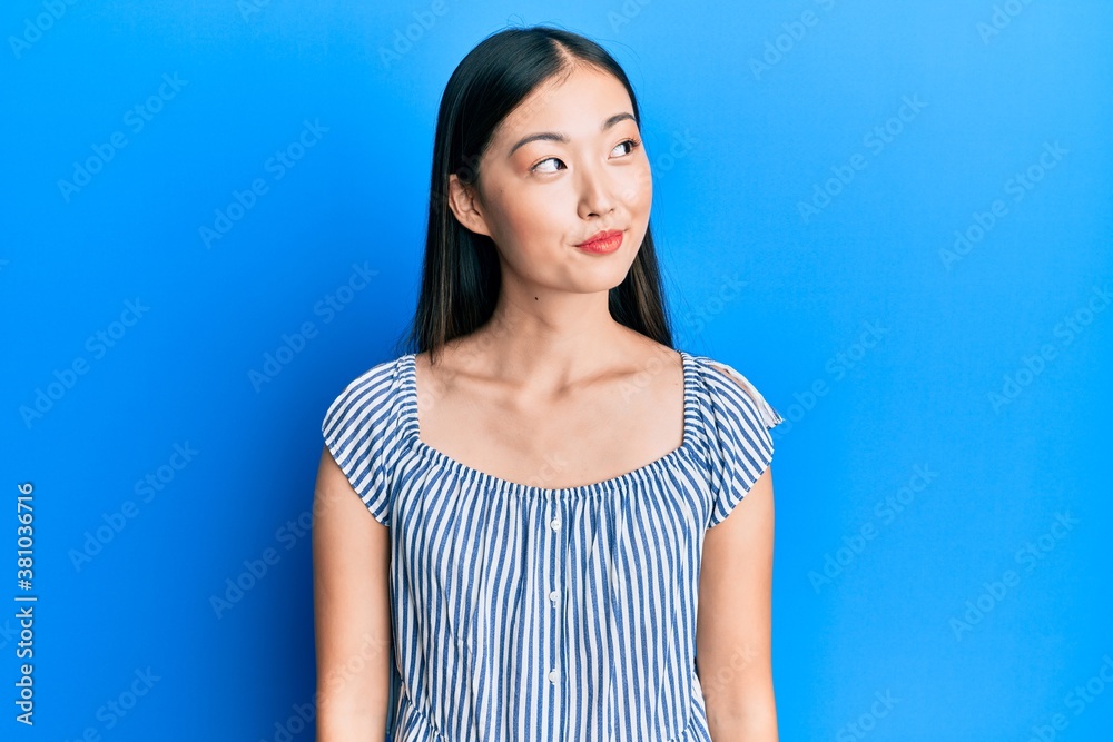 Young chinese woman wearing casual striped t-shirt smiling looking to the side and staring away thinking.