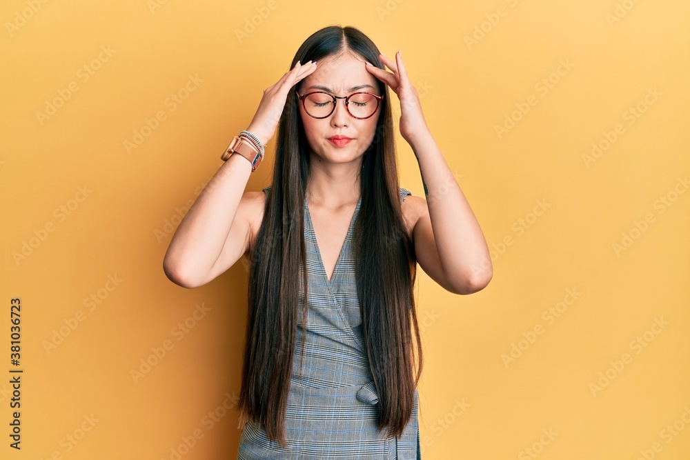 Young chinese woman wearing business dress and glasses with hand on head, headache because stress. suffering migraine. Young chinese woman wearing business dress and glasses with hand on head, headache because stress. suffering migraine.
