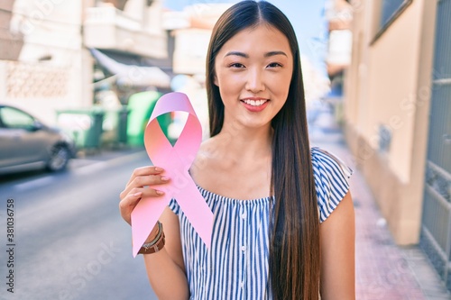 Young chinese woman smiling happy holding pink ribbon at street of city.