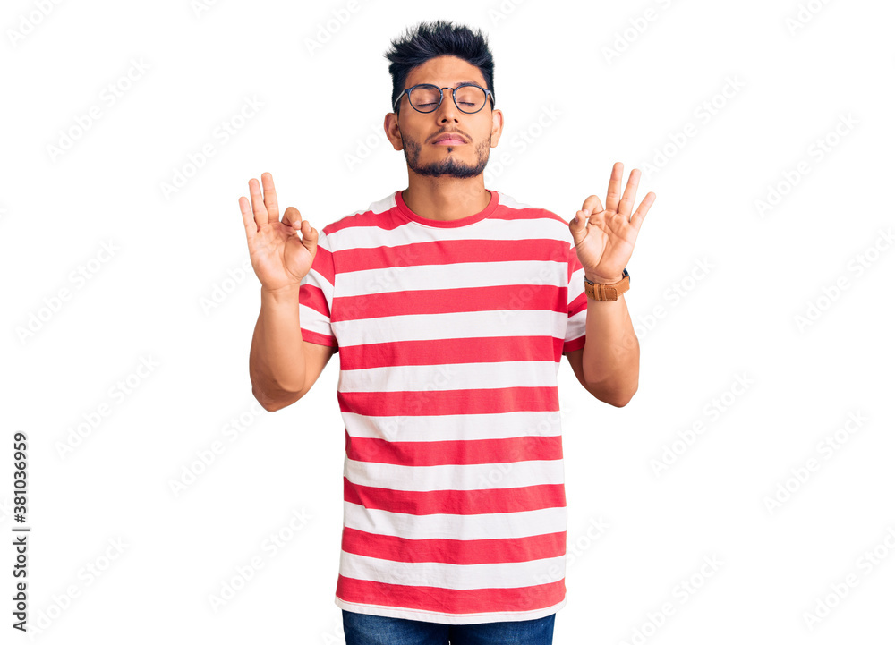 Handsome latin american young man wearing casual clothes and glasses relaxed and smiling with eyes closed doing meditation gesture with fingers. yoga concept. Handsome latin american young man wearing casual clothes and glasses relaxed and smiling with eyes closed doing meditation gesture with fingers. yoga concept.