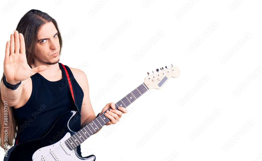 Young adult man with long hair playing electric guitar with open hand doing stop sign with serious and confident expression, defense gesture Young adult man with long hair playing electric guitar with open hand doing stop sign with serious and confident expression, defense gesture