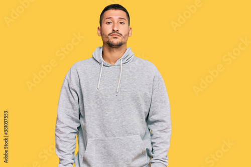 Handsome man with tattoos wearing casual sweatshirt with serious expression on face. simple and natural looking at the camera.