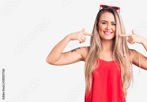Young beautiful blonde woman wearing sleeveless t-shirt and sunglasses smiling cheerful showing and pointing with fingers teeth and mouth. dental health concept.