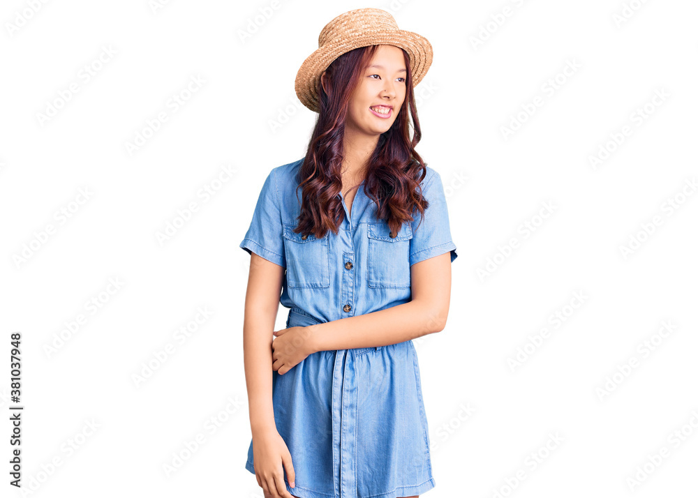 Young beautiful chinese girl wearing summer hat looking away to side with smile on face, natural expression. laughing confident. Young beautiful chinese girl wearing summer hat looking away to side with smile on face, natural expression. laughing confident.