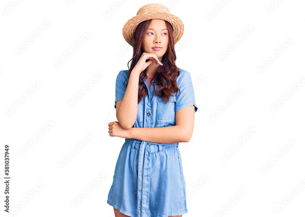 Young beautiful chinese girl wearing summer hat with hand on chin thinking about question, pensive expression. smiling and thoughtful face. doubt concept. Young beautiful chinese girl wearing summer hat with hand on chin thinking about question, pensive expression. smiling and thoughtful face. doubt concept.