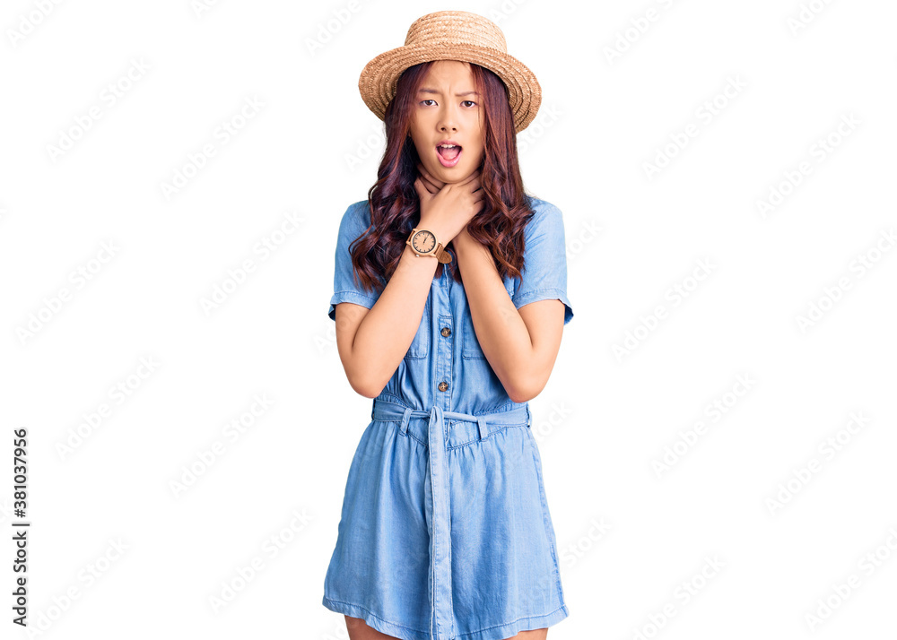 Young beautiful chinese girl wearing summer hat shouting suffocate because painful strangle. health problem. asphyxiate and suicide concept. Young beautiful chinese girl wearing summer hat shouting suffocate because painful strangle. health problem. asphyxiate and suicide concept.