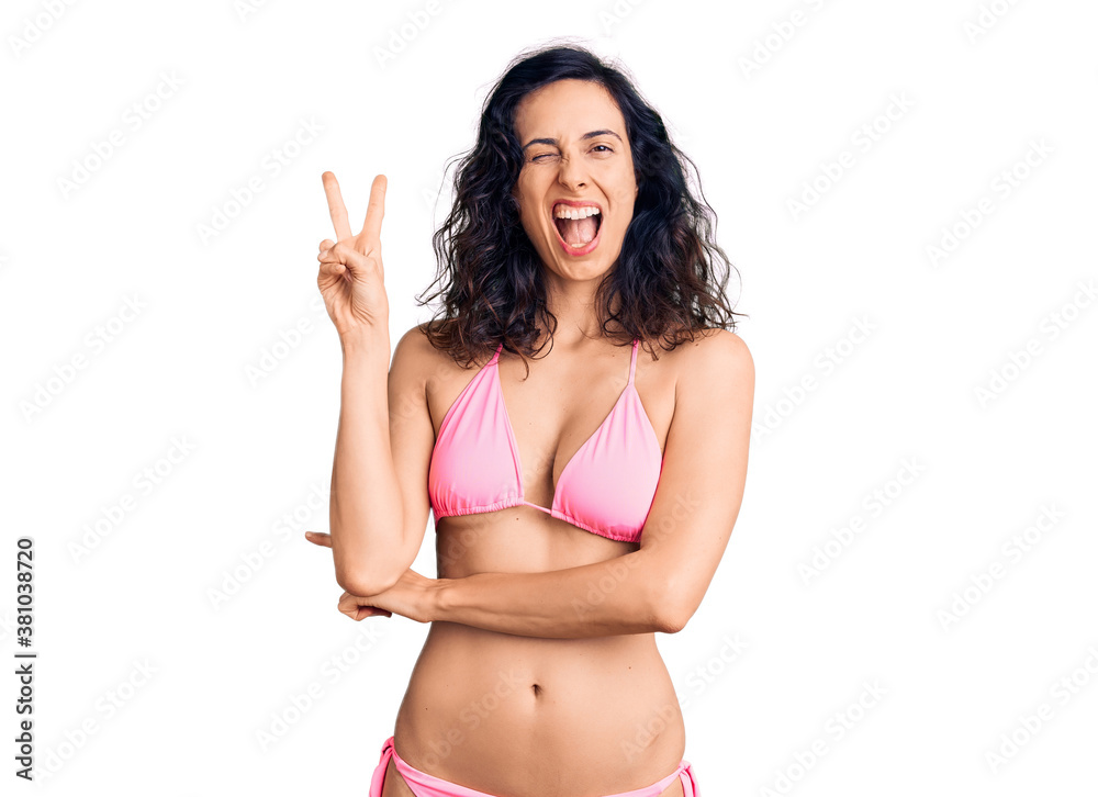 Young beautiful hispanic woman wearing bikini smiling with happy face winking at the camera doing victory sign with fingers. number two. Young beautiful hispanic woman wearing bikini smiling with happy face winking at the camera doing victory sign with fingers. number two.
