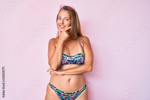 Middle age hispanic woman wearing bikini looking confident at the camera smiling with crossed arms and hand raised on chin. thinking positive.