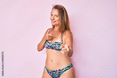 Middle age hispanic woman wearing bikini pointing fingers to camera with happy and funny face. good energy and vibes.