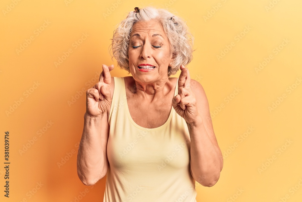Senior grey-haired woman wearing casual clothes gesturing finger crossed smiling with hope and eyes closed. luck and superstitious concept.