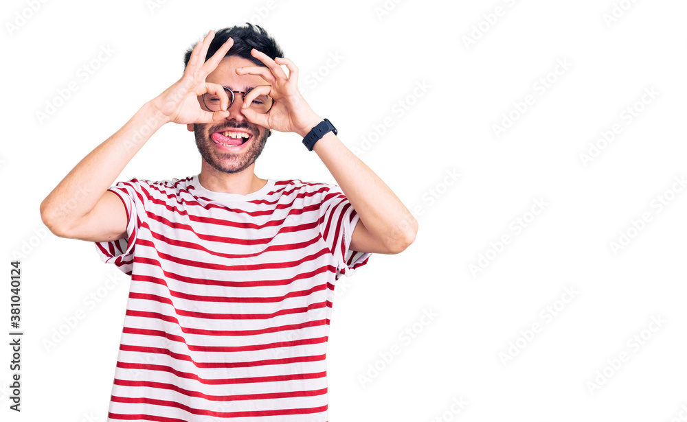 Young hispanic man wearing casual clothes doing ok gesture like binoculars sticking tongue out, eyes looking through fingers. crazy expression. Young hispanic man wearing casual clothes doing ok gesture like binoculars sticking tongue out, eyes looking through fingers. crazy expression.