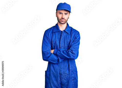 Young hispanic man wearing painter uniform skeptic and nervous, disapproving expression on face with crossed arms. negative person.