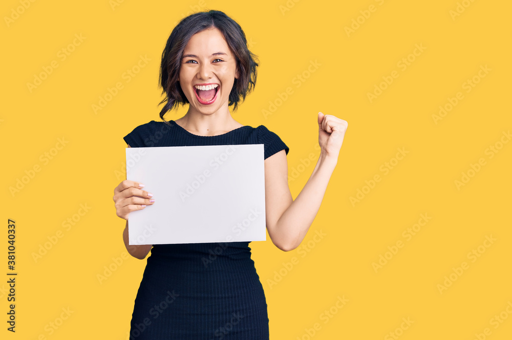 Young beautiful girl holding blank empty banner screaming proud, celebrating victory and success very excited with raised arms Young beautiful girl holding blank empty banner screaming proud, celebrating victory and success very excited with raised arms