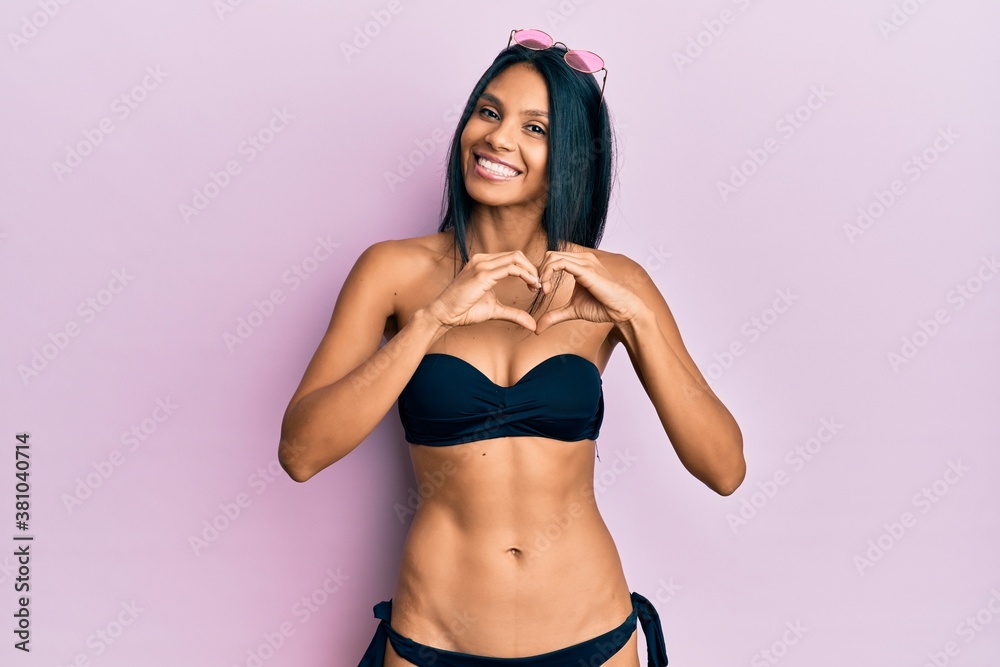 Fototapeta premium Young african american woman wearing bikini smiling in love doing heart symbol shape with hands. romantic concept.