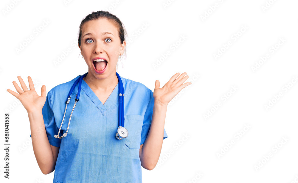 Young beautiful blonde woman wearing doctor uniform and stethoscope celebrating crazy and amazed for success with arms raised and open eyes screaming excited. winner concept Young beautiful blonde woman wearing doctor uniform and stethoscope celebrating crazy and amazed for success with arms raised and open eyes screaming excited. winner concept