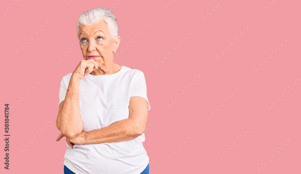 Senior beautiful woman with blue eyes and grey hair wearing casual white tshirt with hand on chin thinking about question, pensive expression. smiling and thoughtful face. doubt concept. Senior beautiful woman with blue eyes and grey hair wearing casual white tshirt with hand on chin thinking about question, pensive expression. smiling and thoughtful face. doubt concept.