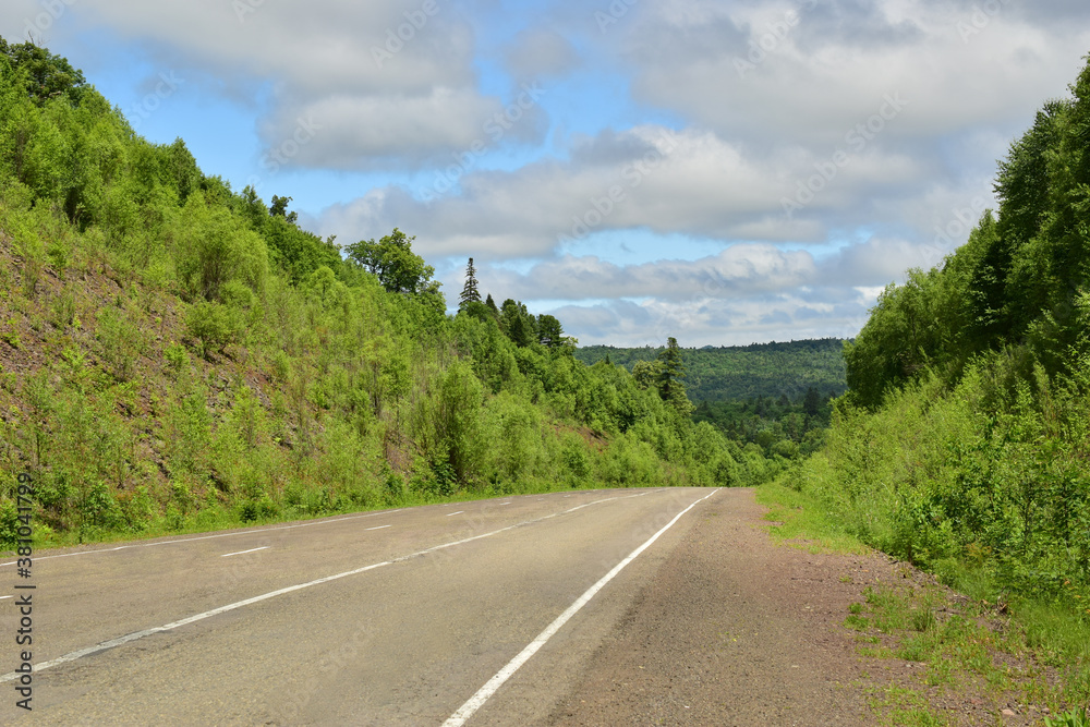 Old asphalt road in the hills. Blue sky with white clouds, green forest on the hills.
