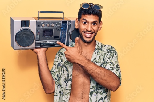 Young latin man wearing summer shirt holding boombox smiling happy pointing with hand and finger