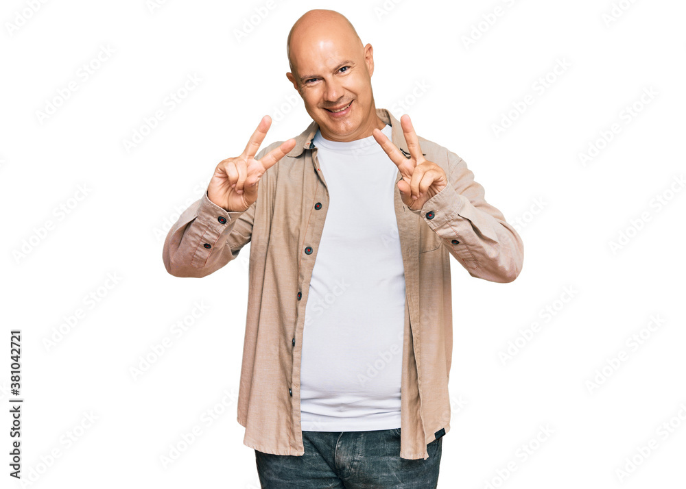 Middle age bald man wearing casual clothes smiling looking to the camera showing fingers doing victory sign. number two. Middle age bald man wearing casual clothes smiling looking to the camera showing fingers doing victory sign. number two.