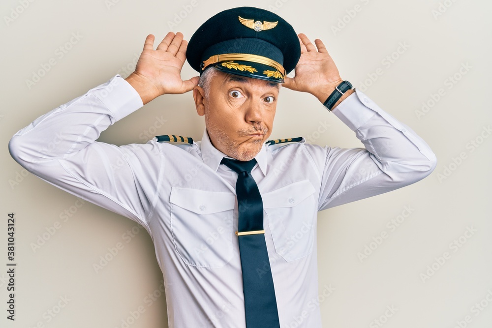 Handsome middle age mature man wearing airplane pilot uniform doing bunny ears gesture with hands palms looking cynical and skeptical. easter rabbit concept. Handsome middle age mature man wearing airplane pilot uniform doing bunny ears gesture with hands palms looking cynical and skeptical. easter rabbit concept.