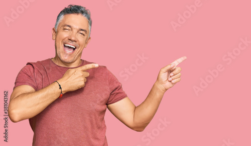 Handsome middle age man wearing casual clothes smiling and looking at the camera pointing with two hands and fingers to the side. © Krakenimages.com