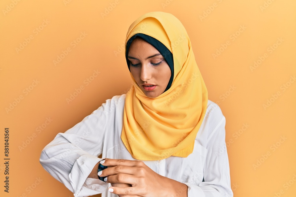 Young brunette arab woman wearing traditional islamic hijab scarf checking the time on wrist watch, relaxed and confident Young brunette arab woman wearing traditional islamic hijab scarf checking the time on wrist watch, relaxed and confident