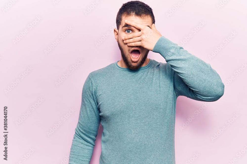 Young handsome man wearing casual sweater peeking in shock covering face and eyes with hand, looking through fingers afraid Young handsome man wearing casual sweater peeking in shock covering face and eyes with hand, looking through fingers afraid
