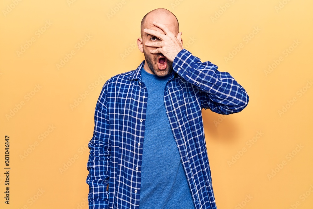Young handsome bald man wearing casual shirt peeking in shock covering face and eyes with hand, looking through fingers afraid Young handsome bald man wearing casual shirt peeking in shock covering face and eyes with hand, looking through fingers afraid