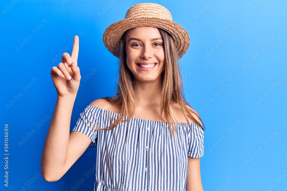 Young beautiful girl wearing summer hat and striped t-shirt smiling with an idea or question pointing finger up with happy face, number one Young beautiful girl wearing summer hat and striped t-shirt smiling with an idea or question pointing finger up with happy face, number one