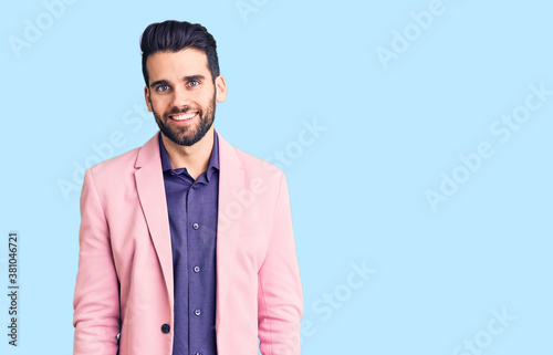 Young handsome man with beard wearing elegant jacket looking positive and happy standing and smiling with a confident smile showing teeth