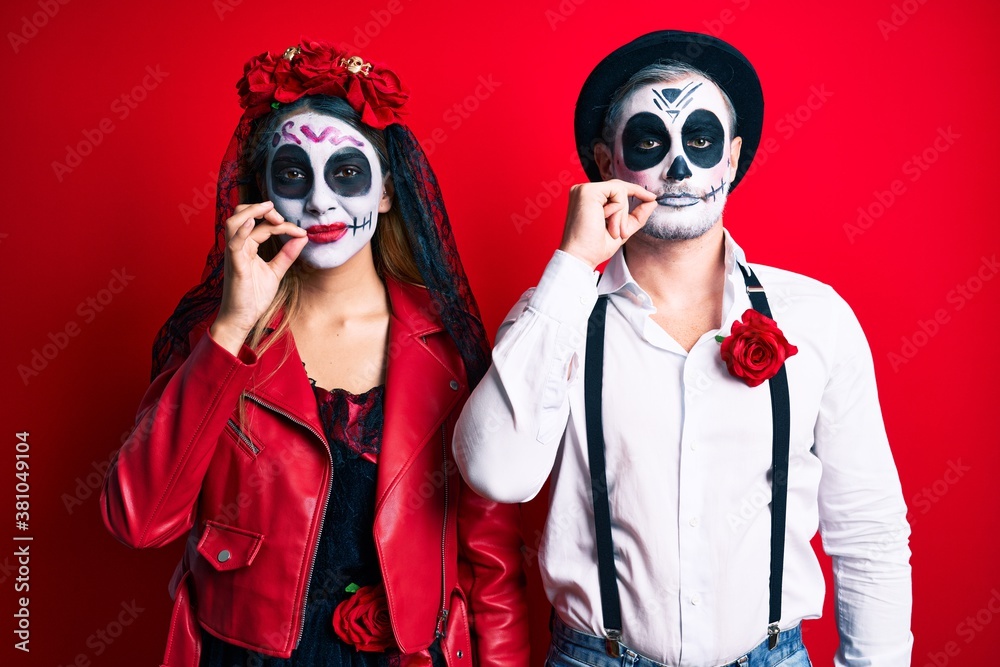 Couple wearing day of the dead costume over red mouth and lips shut as zip with fingers. secret and silent, taboo talking Couple wearing day of the dead costume over red mouth and lips shut as zip with fingers. secret and silent, taboo talking