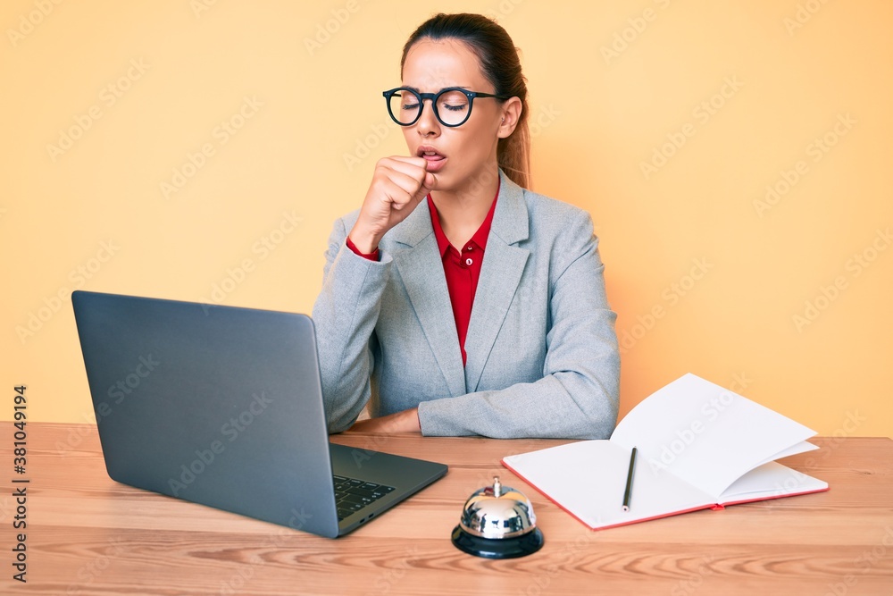 Young brunette woman working at hotel reception using laptop feeling unwell and coughing as symptom for cold or bronchitis. health care concept. - obrazy, fototapety, plakaty 