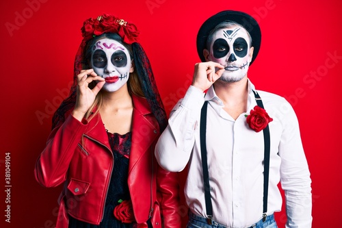 Couple wearing day of the dead costume over red mouth and lips shut as zip with fingers. secret and silent  taboo talking