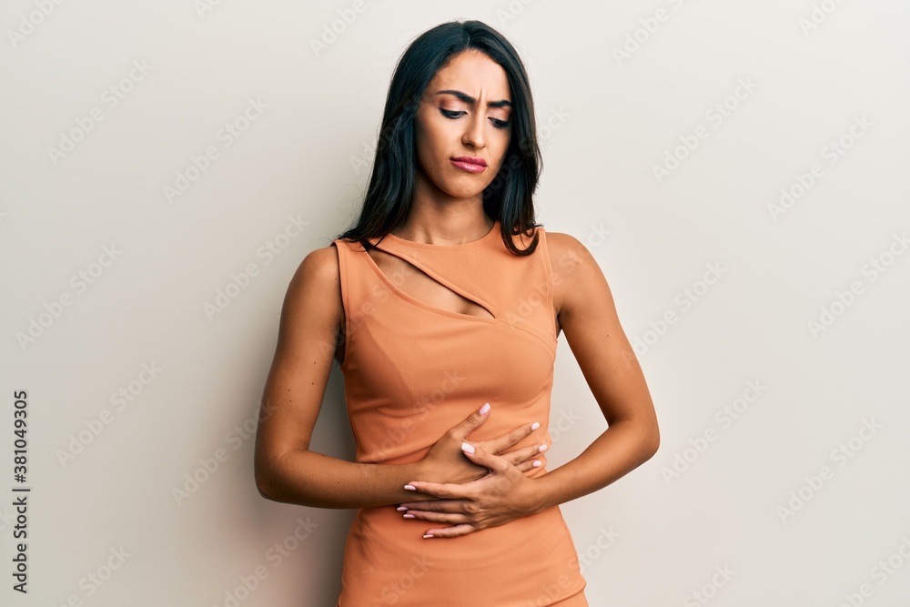 Beautiful hispanic woman wearing summer dress with hand on stomach because indigestion, painful illness feeling unwell. ache concept.