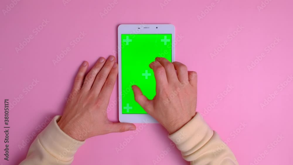 Top view - Hands of unrecognizable person using digital table with green screen on pink background. Creative background. Male hands scrolling pages, tapping on touch screen. Chroma key. Top view - Hands of unrecognizable person using digital table with green screen on pink background. Creative background. Male hands scrolling pages, tapping on touch screen. Chroma key.