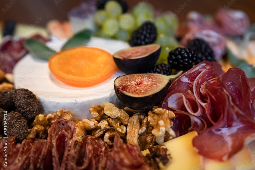 Food board with cured meats prosciutto, salami and coppa, hard and soft cheeses brie, cheddar, gouda, emmental and figs, grapes, blueberries, blackberries, candied orange decorated with sage leaves