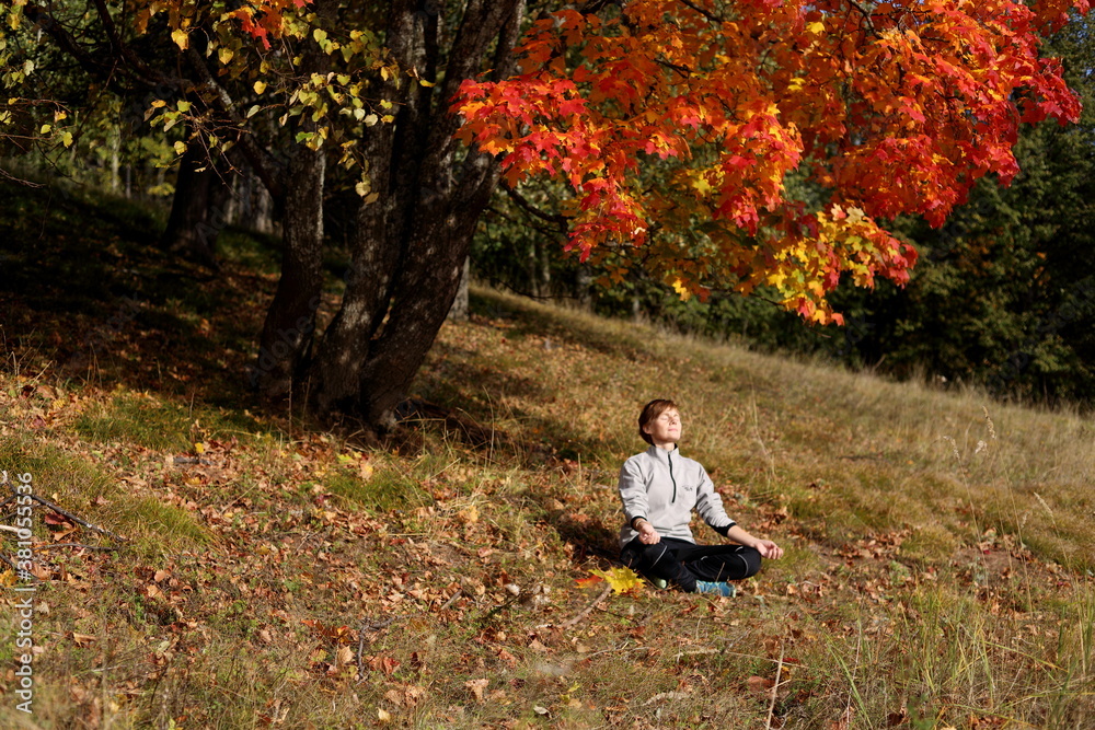 Girl meditates under an autumn tree with bright yellow and red leaves Girl meditates under an autumn tree with bright yellow and red leaves