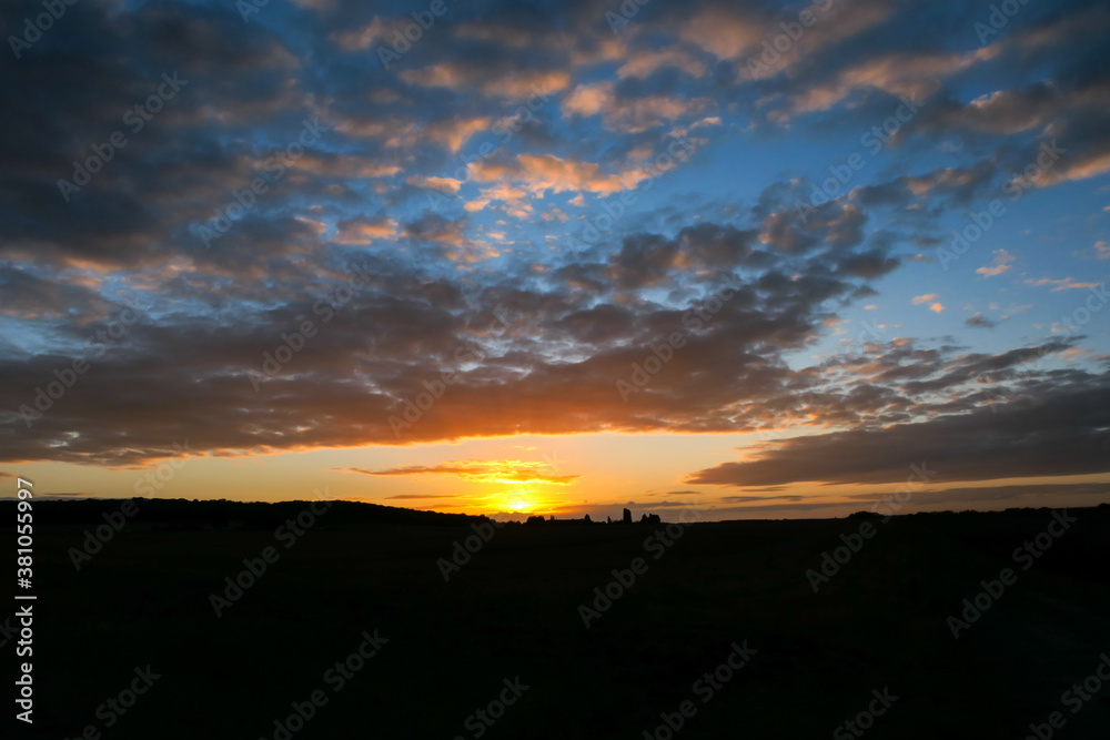 Obraz premium Amazing sunset in the countryside. Cumulonimbus and very colorful stratus in a dramatic sky. Sun disappearing behind a hill.