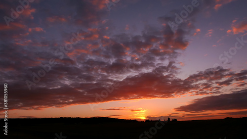 Amazing sunset in the countryside. Cumulonimbus and very colorful stratus in a dramatic sky. Sun disappearing behind a hill.