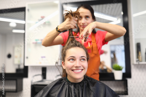 Female client sits in chair in a hairdressing salon. The master holds hair and scissors. Hairdressing training concept