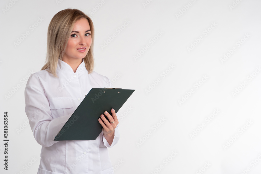 A girl in a medical gown with a notebook in her hand. Female doctor on a white background. Place for text. Medication. Receiving patients. Doctor's recommendation. A girl in a medical gown with a notebook in her hand. Female doctor on a white background. Place for text. Medication. Receiving patients. Doctor's recommendation.