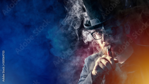 A man in a top hat smokes an electronic cigarette and looks at the camera. VAPE shop. Vaper on a dark background. Place for the text. A serious man with an e-cigarette.