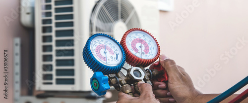 Air repair mechanic using measuring pressure gauge equipment for filling home air conditioner after cleaners and checking maintenance outdoor air compressor unit. photo