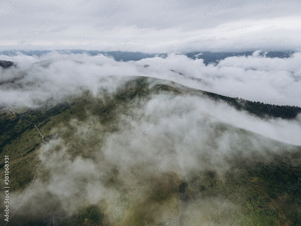 White clouds in the mountains. Clouds are above it and trees on the hill.