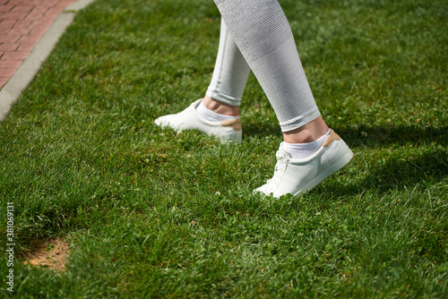 Young woman in white sneakers on the grass. Close-up view of sneakers.