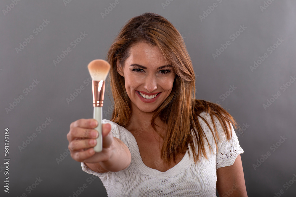 Portrait of beautiful happy woman with make up brush on gray background Portrait of beautiful happy woman with make up brush on gray background
