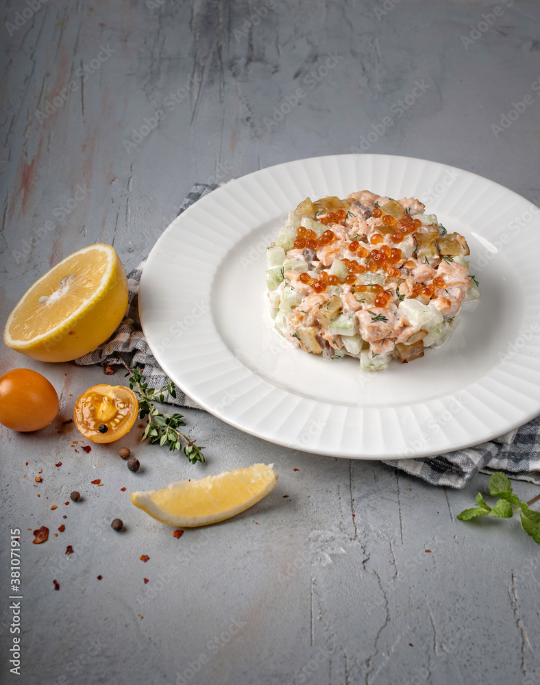 food photography of winter vegetable salad olivier with meat, pickled cucumbers with mayonnaise and red caviar side view on a gray background close up