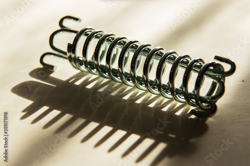 Shiny, strong metal spring and its shadow on a light background