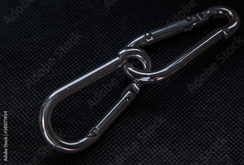 Two metal, interconnected shiny carabiners on a black patterned background